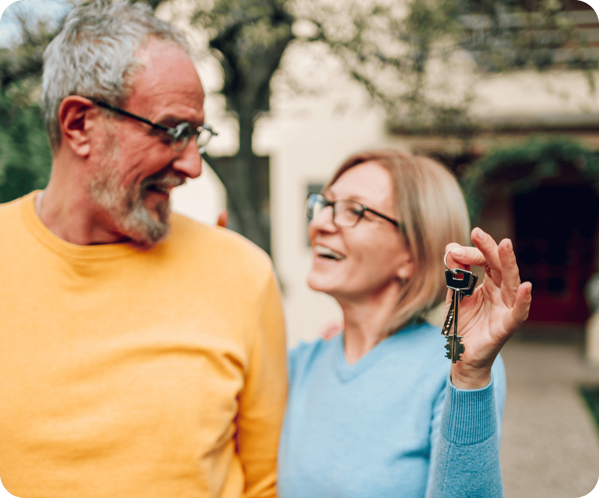 Senior couple holding up new house key while standing outside